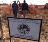 A sign in the foreground and two people walk towards a construction site