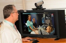 A doctor watches nurse perform an ultrasound via a video screen with a live feed