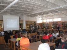 Students in school library view PowerPoint on computer skills